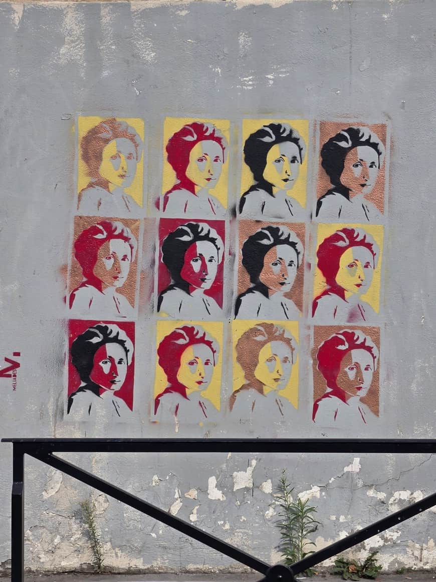 Douze portraits au pochoir répétés en rouge, noir, cuivre et jaune sur un mur gris