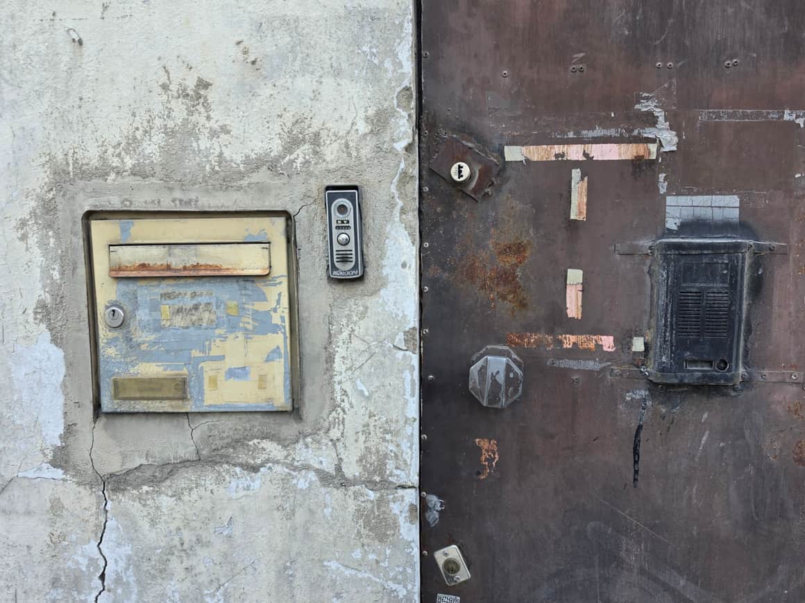 Boîtes aux lettres et interphones fixés sur un mur fissuré et une porte métallique