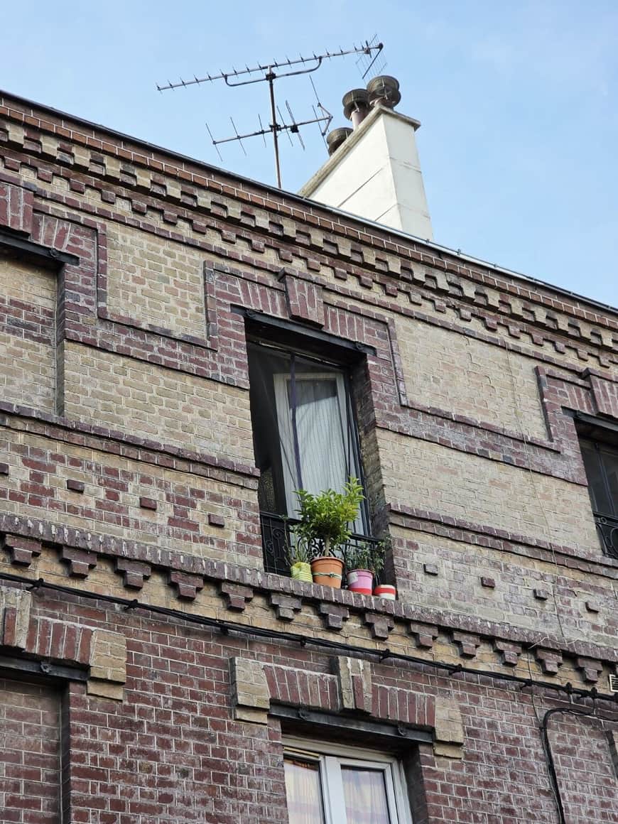 Façade de brique polychrome avec fenêtre, pots de plantes, cheminée et antennes