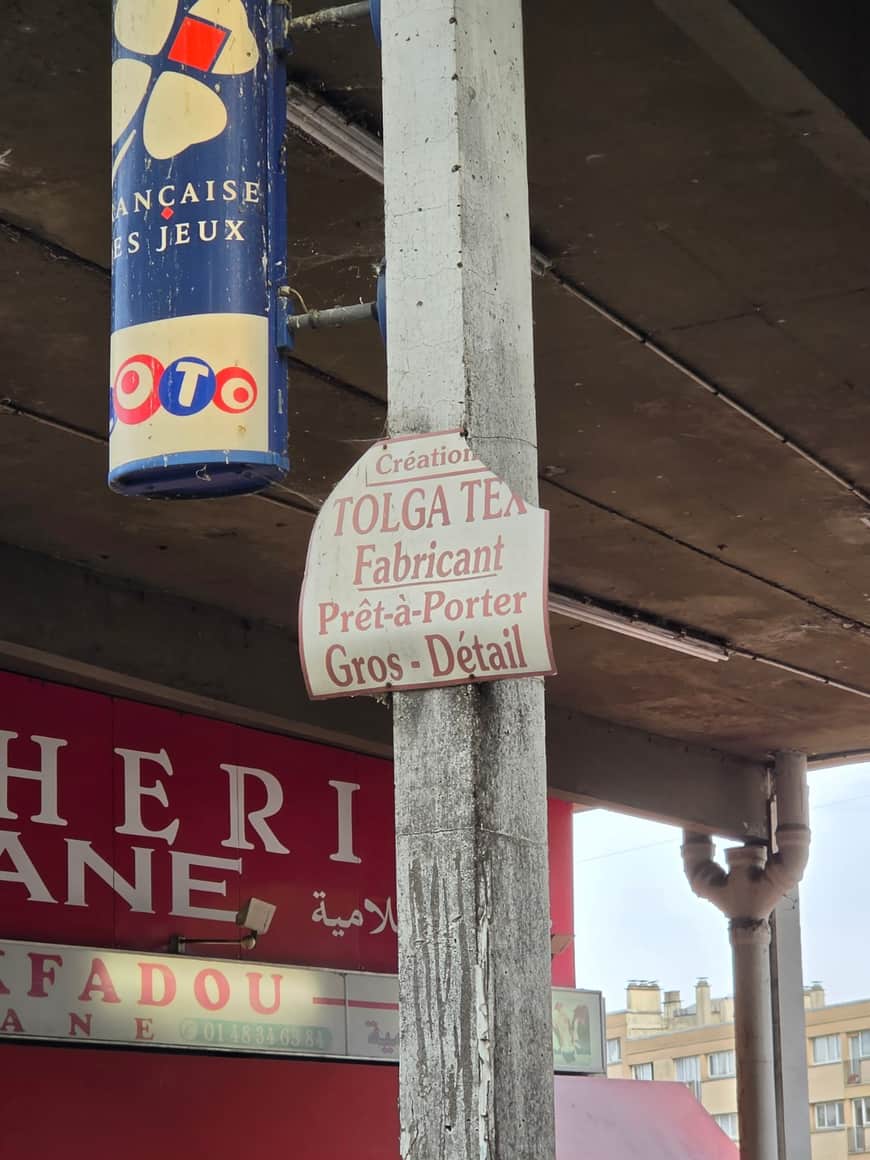 Enseignes de la Française des jeux, du Loto et d’un fabricant de prêt-à-porter fixées autour d’un pilier de béton sous une dalle
