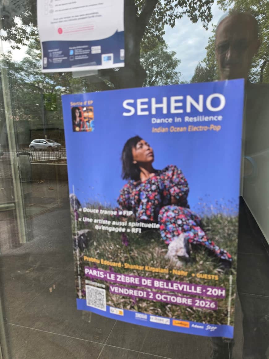 Affiche bleue de Seheno derrière une vitre où se reflètent le photographe, des arbres et une voiture
