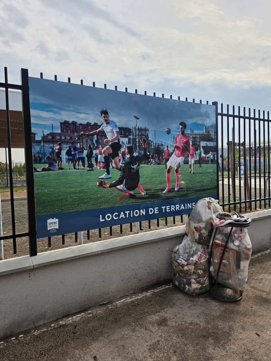 Panneau publicitaire de location de terrains de football avec sacs de déchets à son pied
