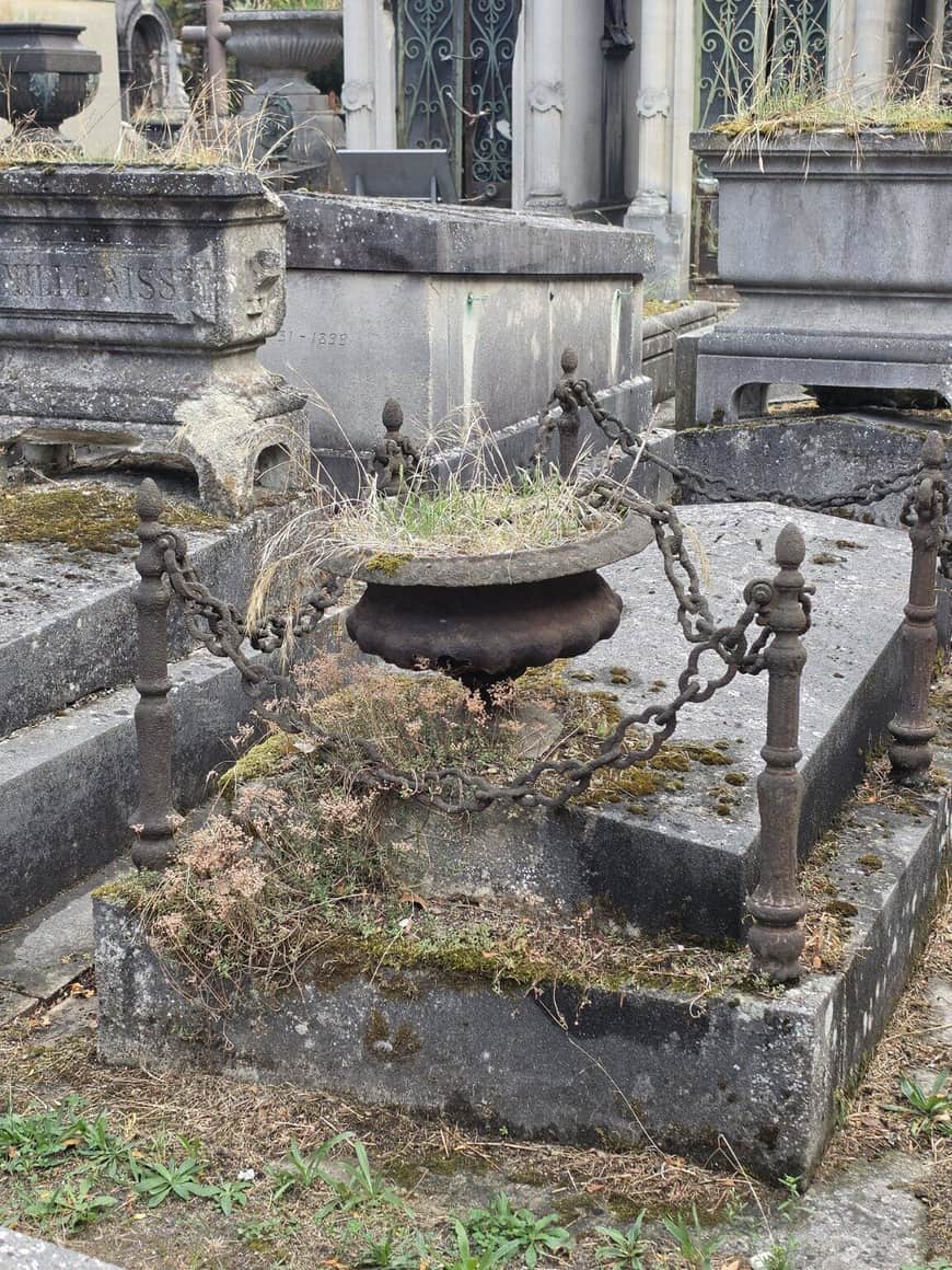 Tombe ancienne ceinte de chaînes, avec urne et végétation spontanée