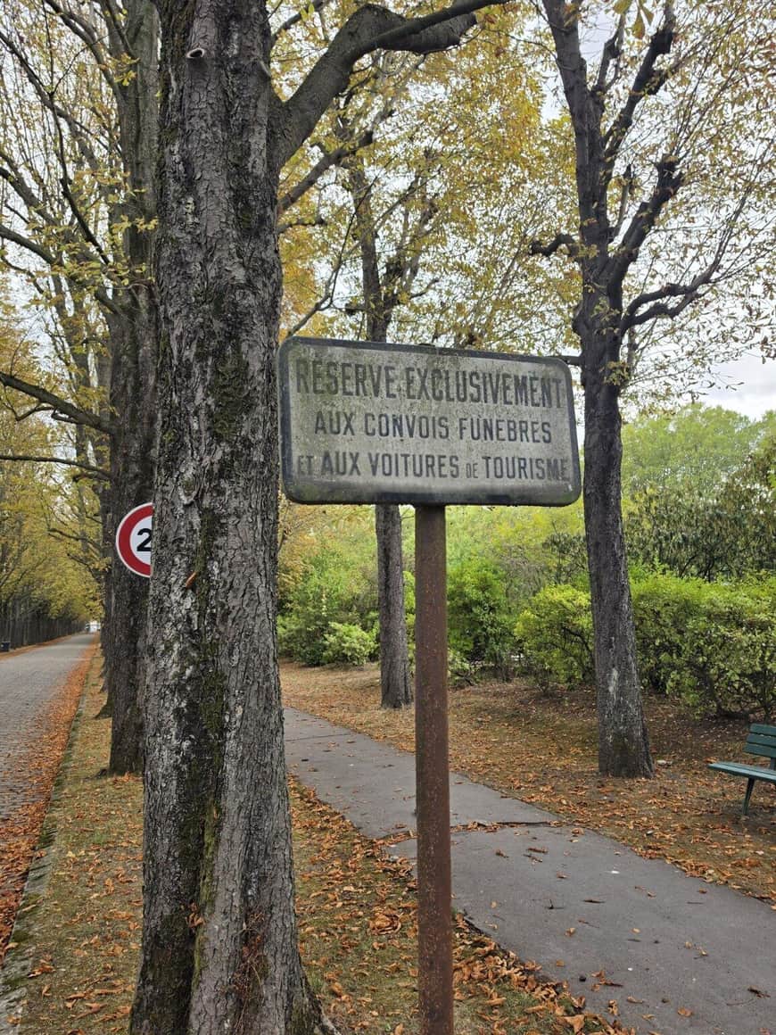 Ancien panneau dans une allée arborée réservant la voie aux convois funèbres et aux voitures de tourisme