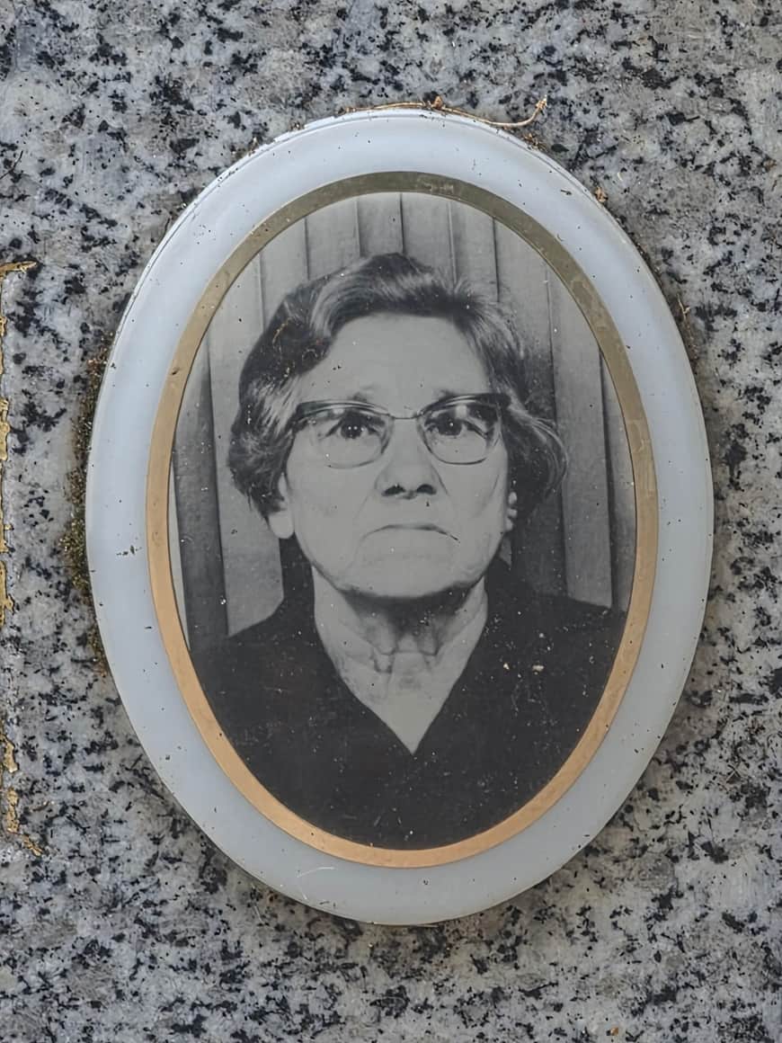 Portrait funéraire ovale en noir et blanc d’une femme portant des lunettes, fixé sur une pierre mouchetée