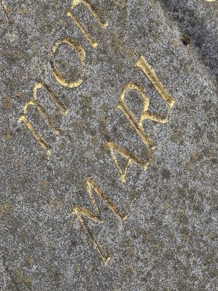 Très gros plan sur des fragments de lettres dorées gravées dans une pierre sombre altérée