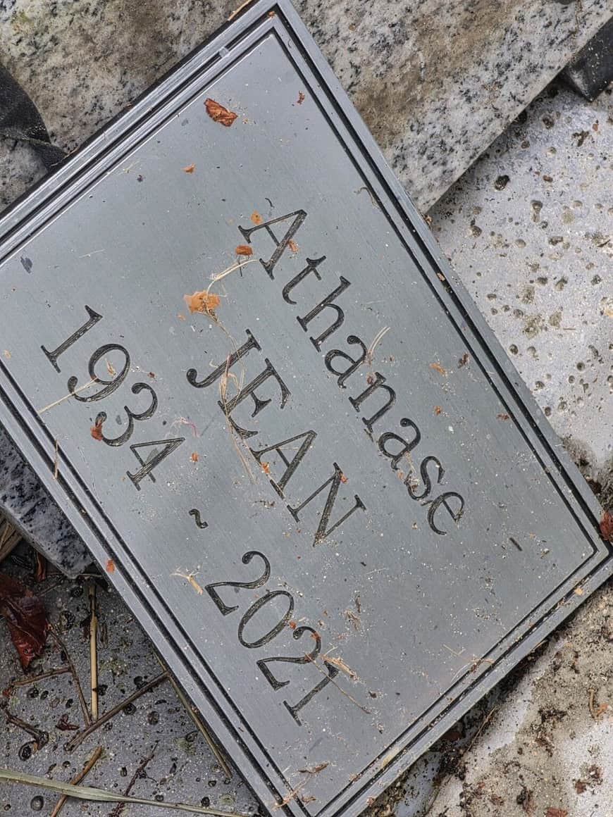 Plaque funéraire métallique portant le nom Athanase Jean et les dates 1934–2021, posée de biais sur une dalle