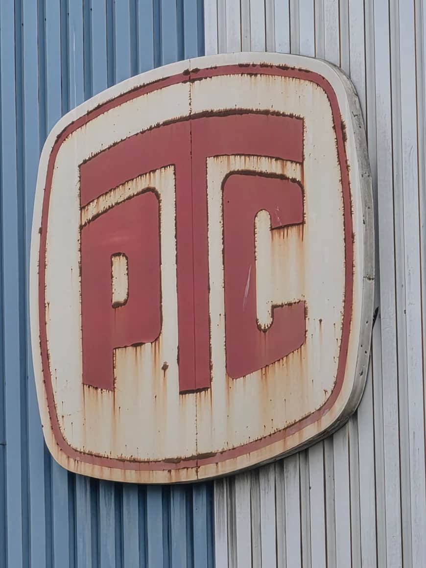 Ancien sigle industriel rouge et blanc, très rouillé, fixé sur un bardage métallique bleu et gris