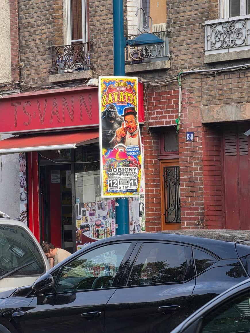 Affiche colorée du cirque Zavatta fixée sur un poteau devant un commerce et des immeubles de brique