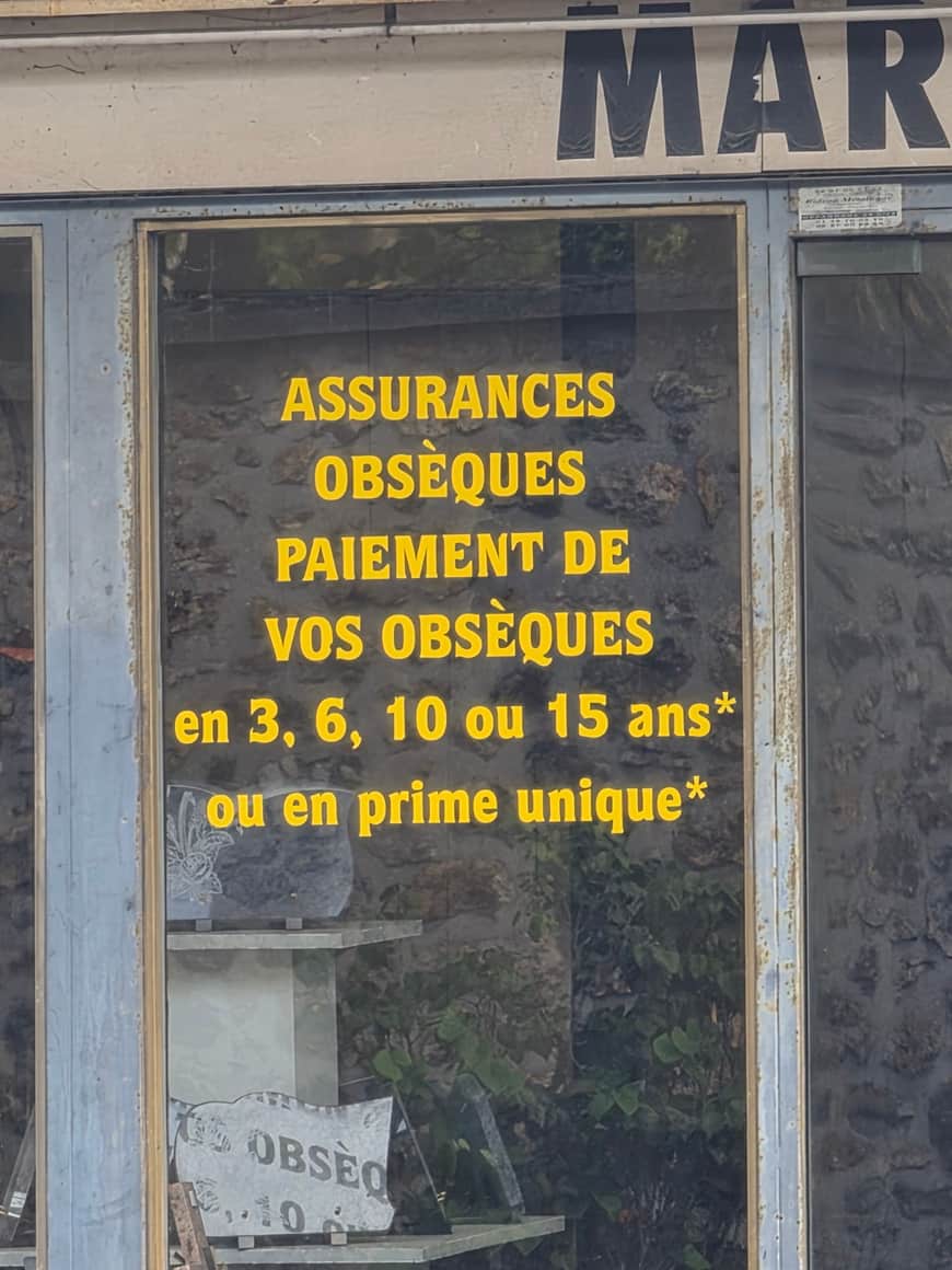 Vitrine annonçant en lettres jaunes des assurances obsèques et le paiement des obsèques sur plusieurs années