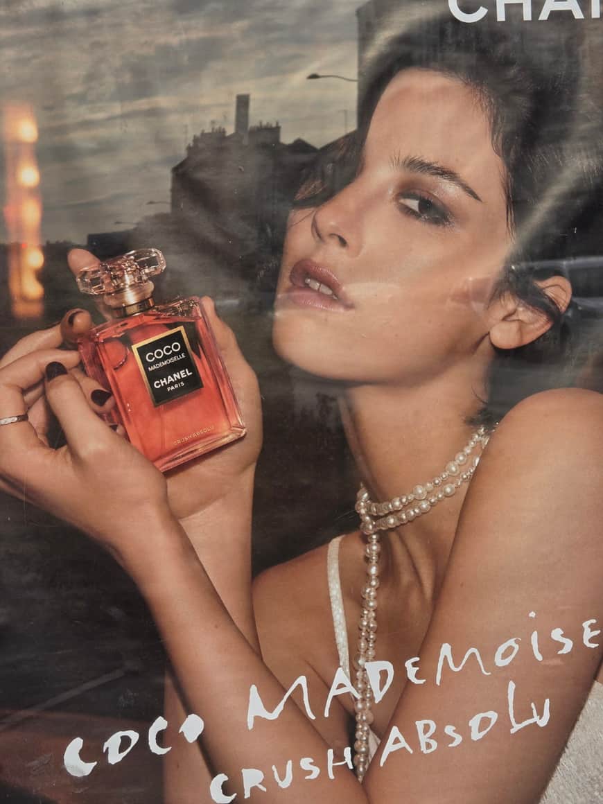 Publicité pour le parfum Coco Mademoiselle de Chanel photographiée derrière une vitre reflétant la rue et le ciel