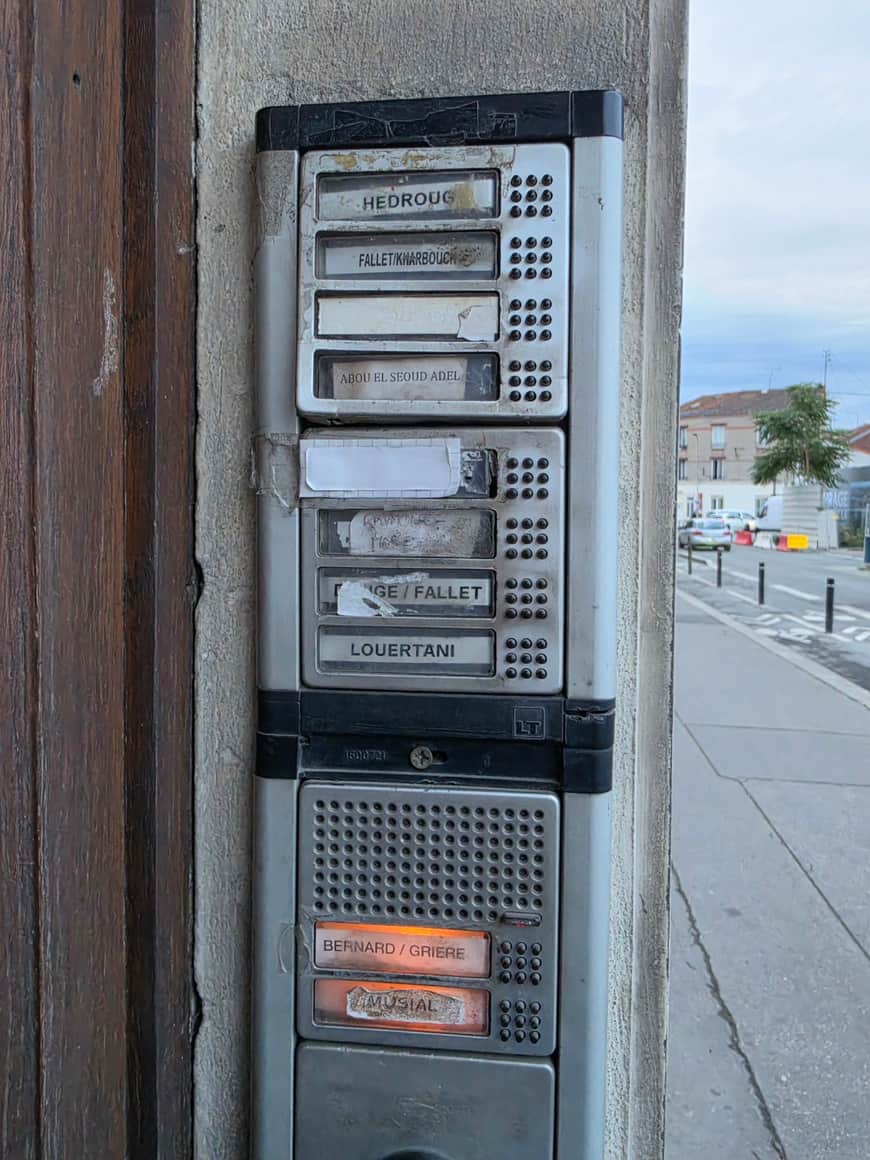Seconde vue rapprochée du même interphone collectif ancien, portant plusieurs étiquettes superposées