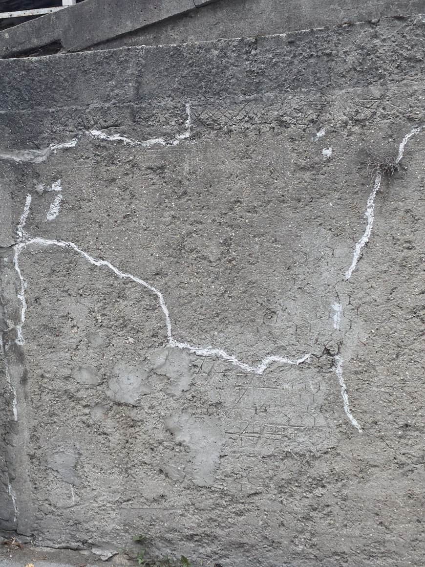 Mur gris fissuré dont plusieurs fractures ont été soulignées ou reprises par des lignes blanches