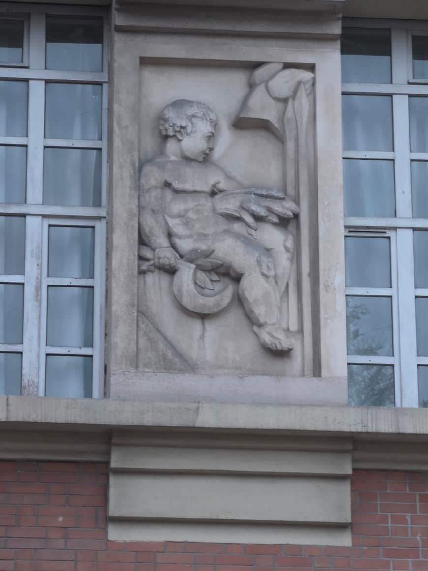 Relief de pierre représentant une jeune figure assise tenant un long outil et un élément circulaire