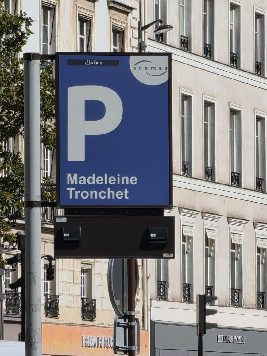 Panneau bleu du parc de stationnement Madeleine Tronchet devant des façades parisiennes