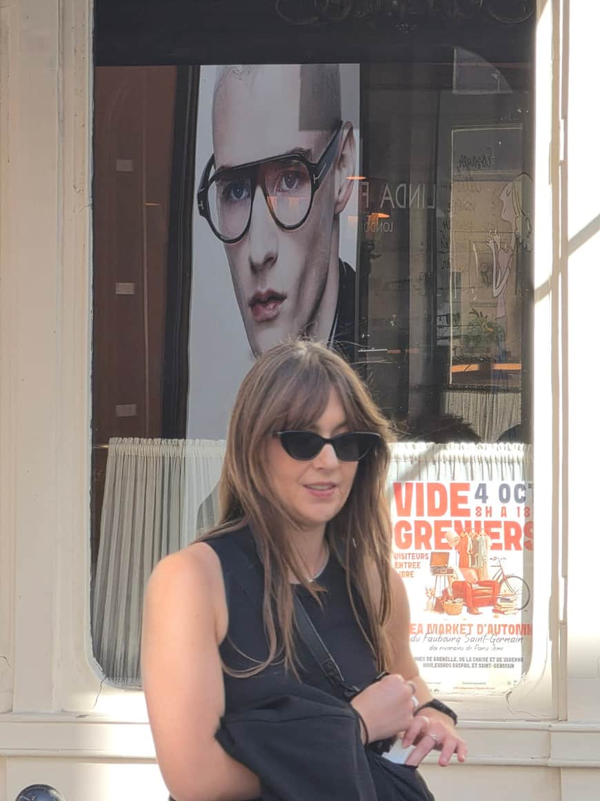 Femme portant des lunettes noires devant une vitrine montrant un homme à lunettes sur une affiche