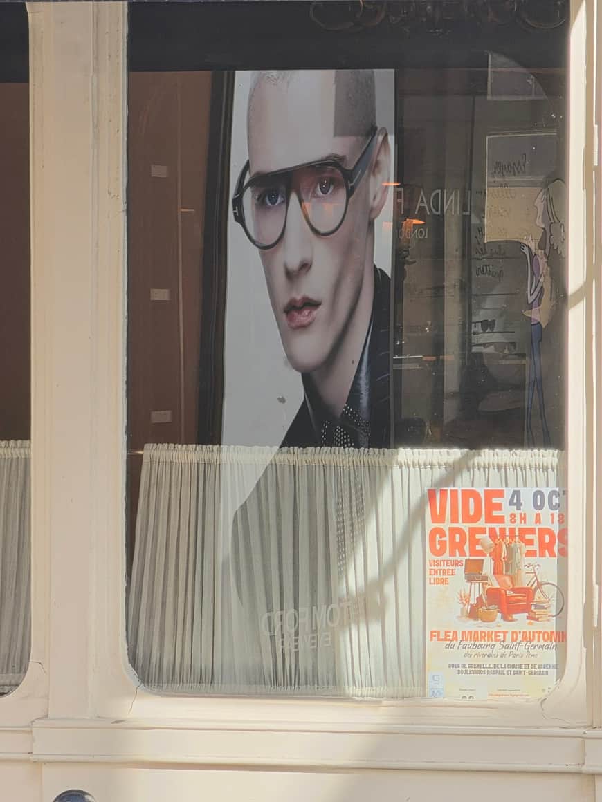 Portrait publicitaire dans une vitrine à côté d’une affiche annonçant un vide-greniers du faubourg Saint-Germain