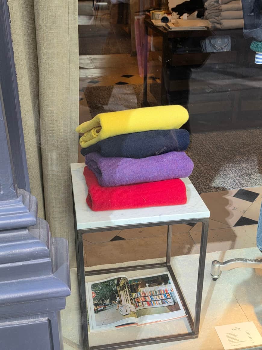 Quatre lainages pliés jaune, bleu, violet et rouge dans une vitrine