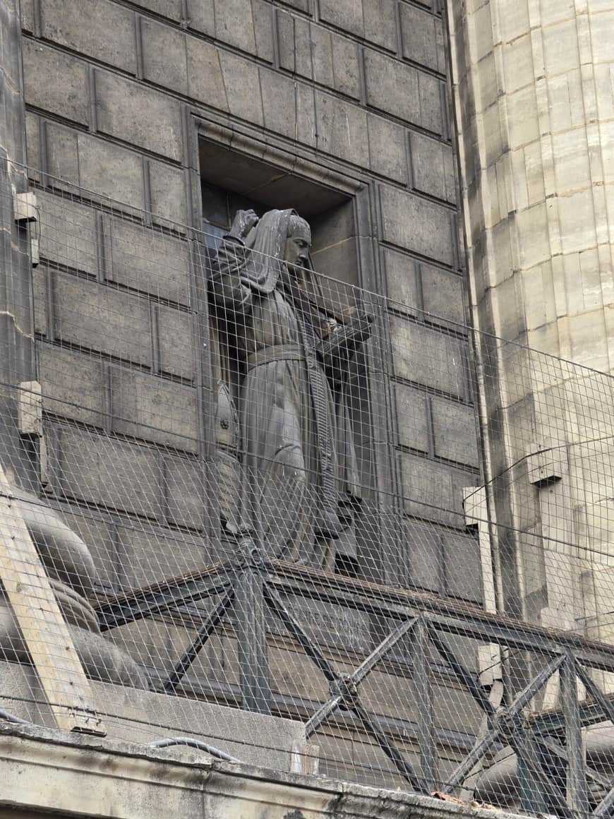 Statue monumentale dans une niche de pierre derrière plusieurs épaisseurs de grillage