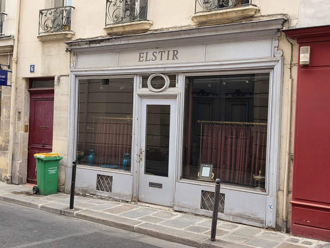 Devanture grise portant le nom Elstir, encadrée de portes rouges et de fenêtres à garde-corps