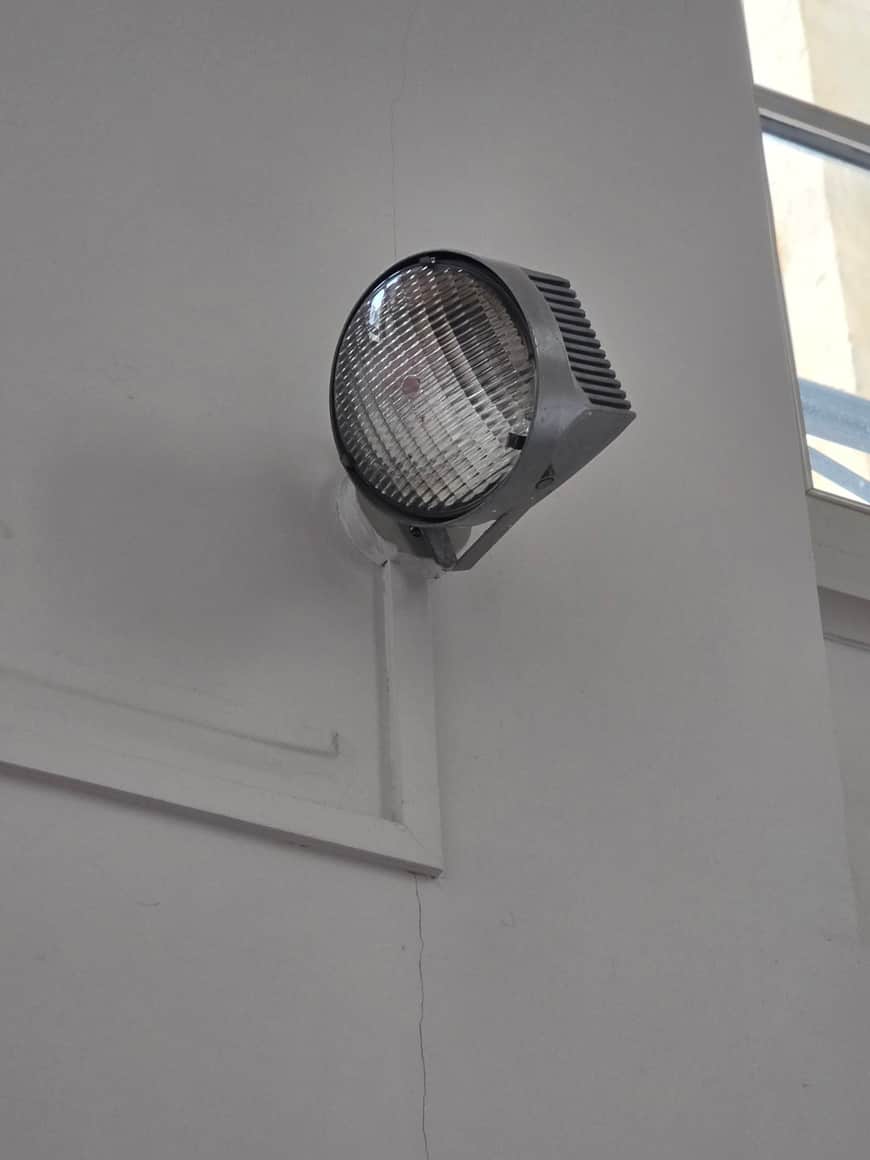 Projecteur rond fixé sur un mur clair traversé de fines fissures