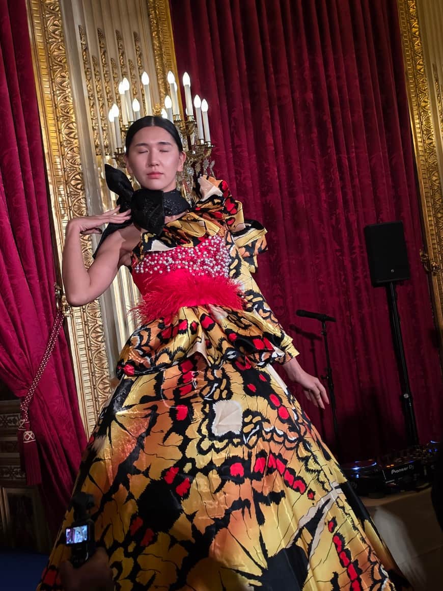 Modèle levant une main dans une ample robe imprimée devant un rideau rouge