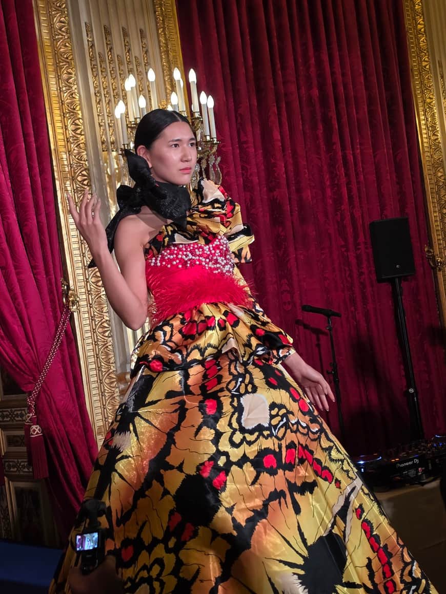 Modèle posant dans une ample robe imprimée orange et noire ornée de plumes roses et de perles