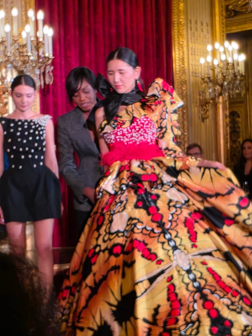 Modèle déployant une ample robe imprimée orange, noire et rose dans un salon doré