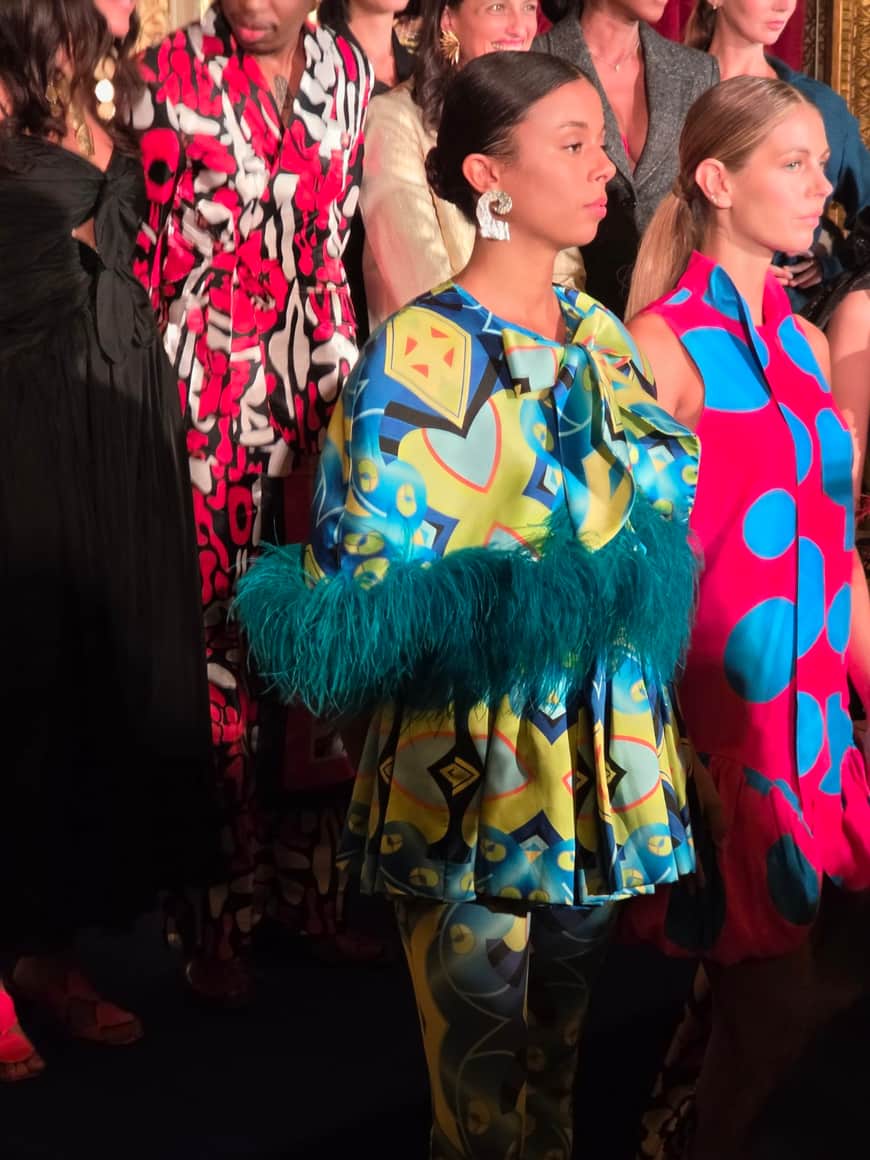 Deux modèles de profil portant des vêtements bleu, vert et rose, dont une tenue bordée de plumes turquoise