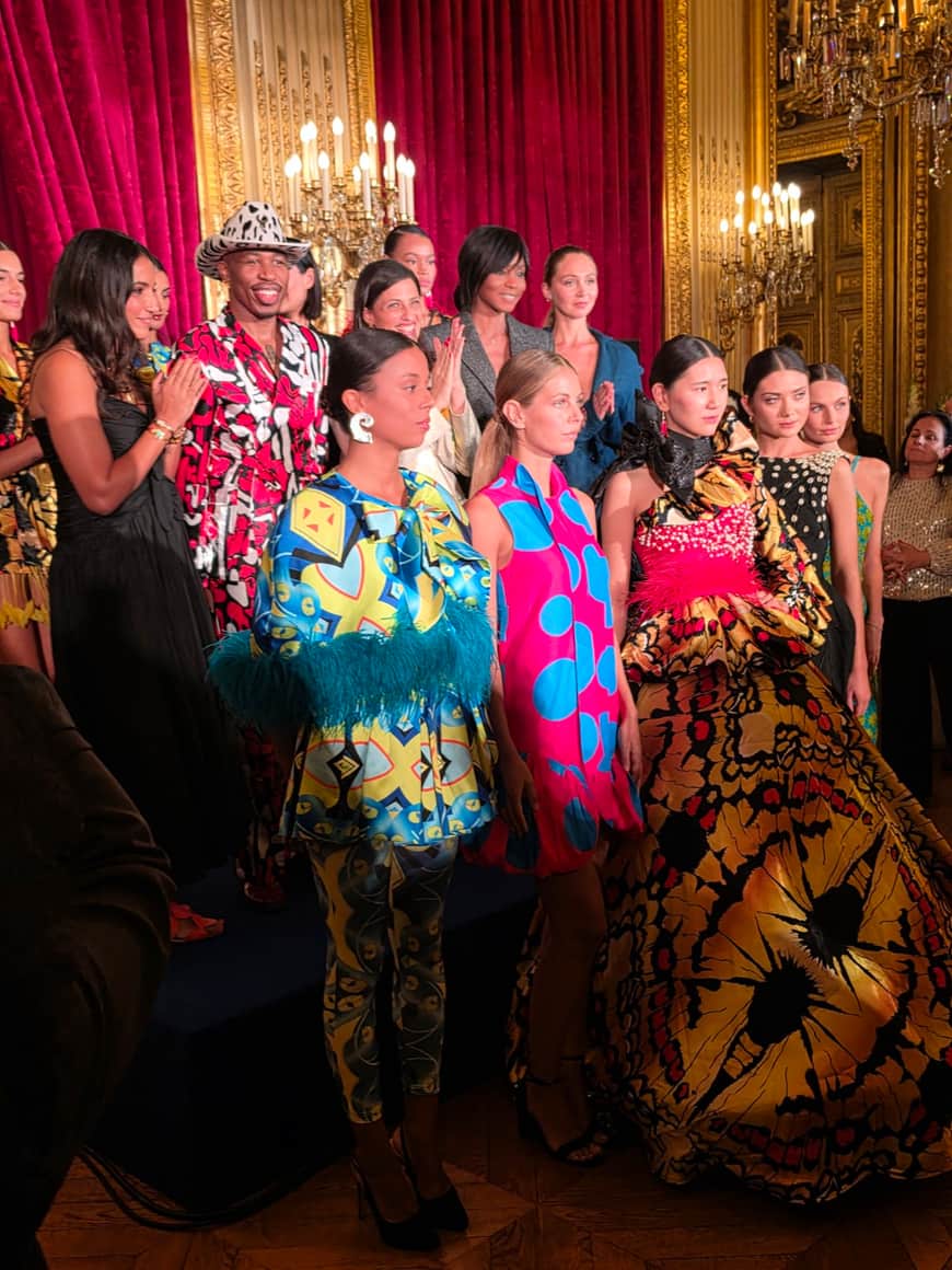 Groupe présentant des vêtements aux motifs colorés dans un salon à velours rouge, dorures et luminaires