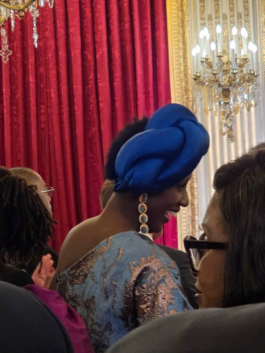 Personne de profil portant un couvre-chef bleu, de longues boucles assorties et un vêtement bleu brodé