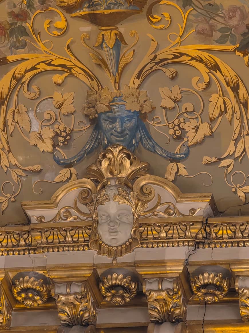Deux mascarons superposés parmi des rinceaux dorés, des grappes et des feuilles sculptées