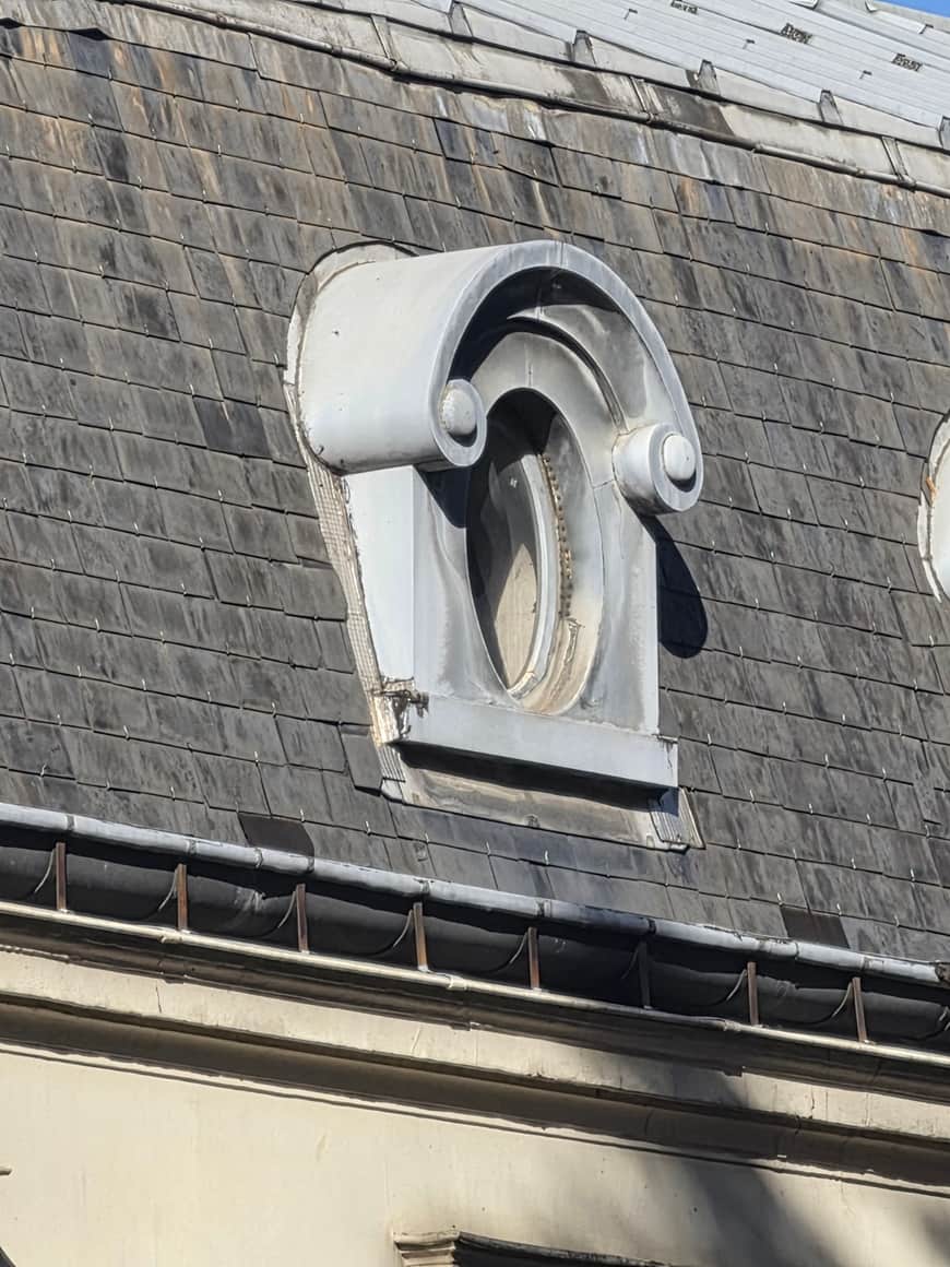 Œil-de-bœuf dans un cartouche à volutes sur une couverture d’ardoise