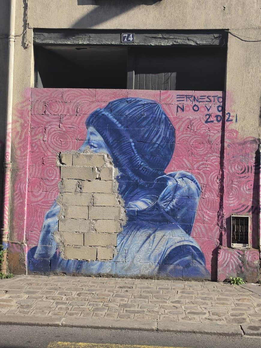 Fresque bleue et rose signée Ernesto Novo en 2021, partiellement recouverte par des parpaings