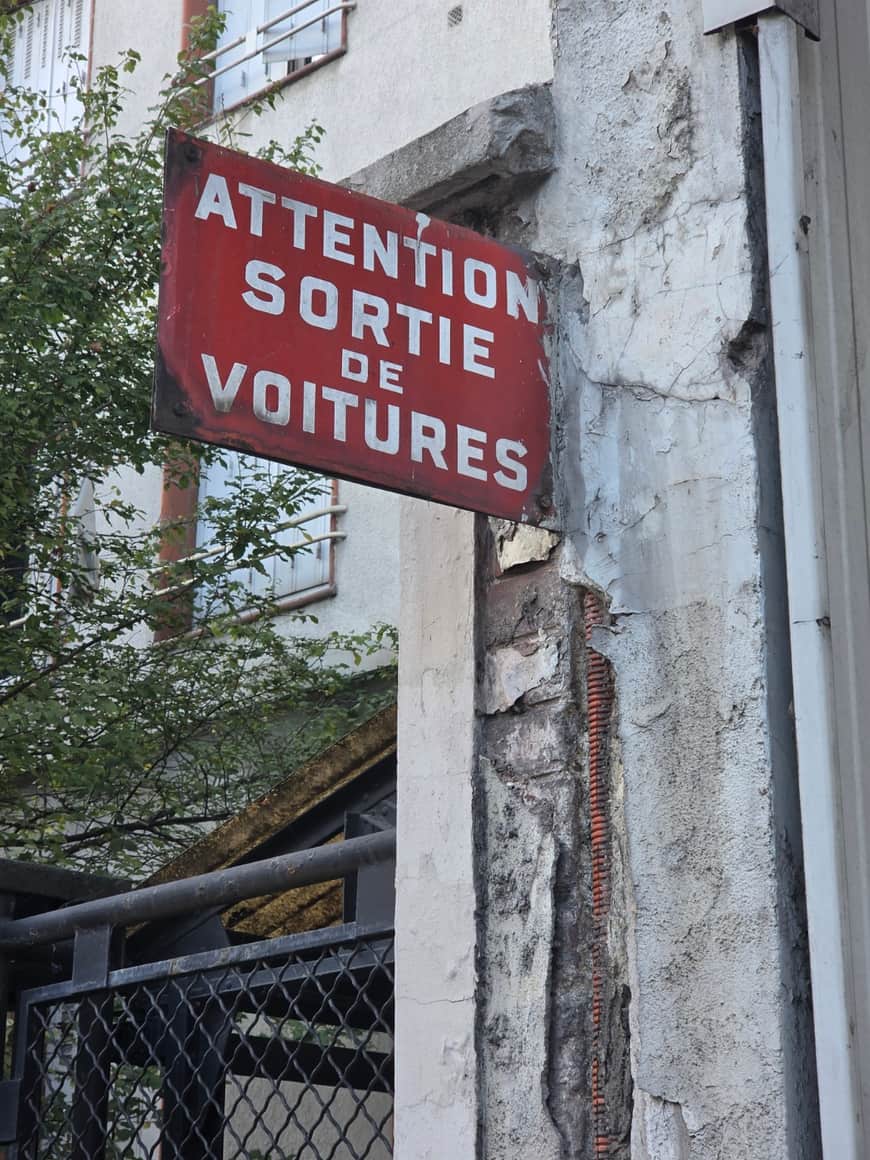 Panneau rouge « Attention sortie voitures » fixé sur un mur.