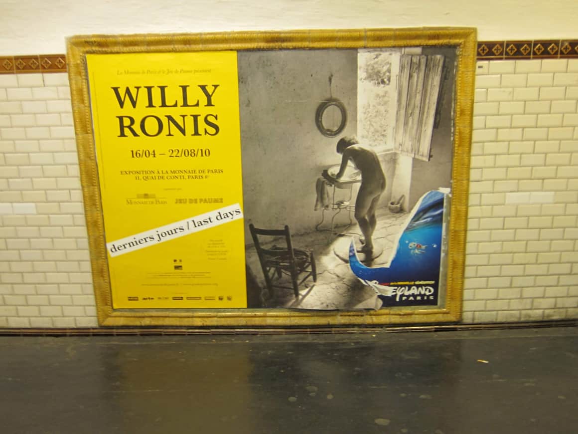 Affiche Willy Ronis traversée par un élément publicitaire bleu.