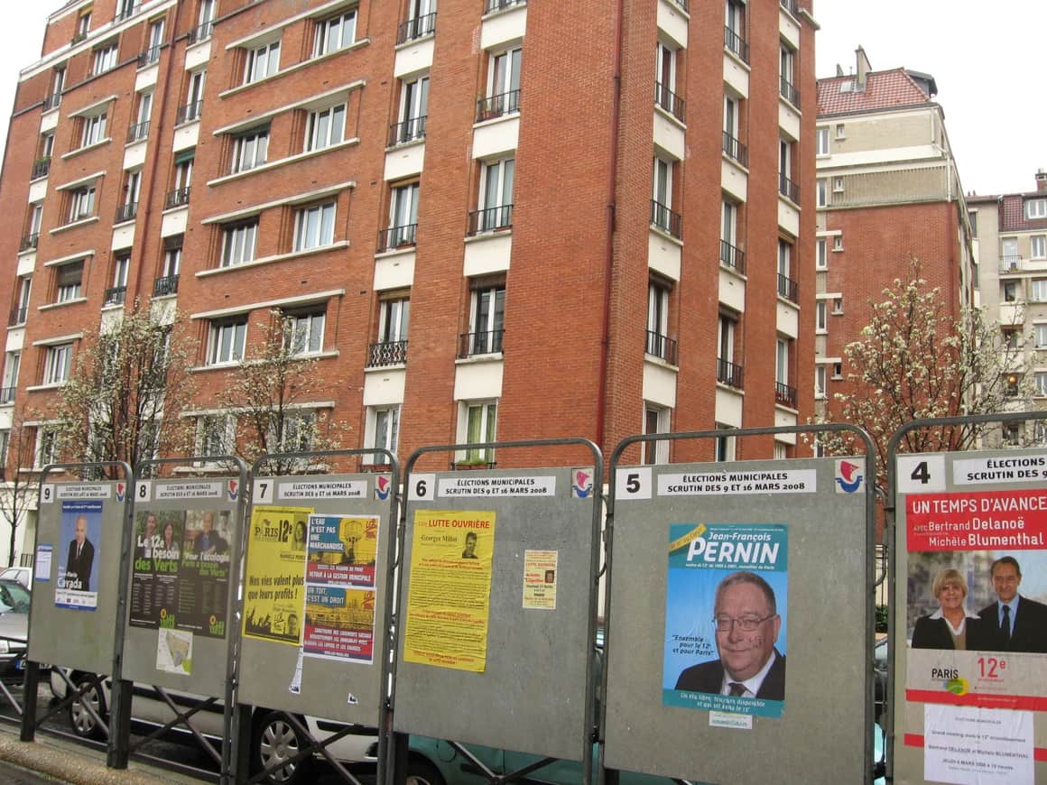 Panneaux de campagne électorale devant un immeuble de briques.