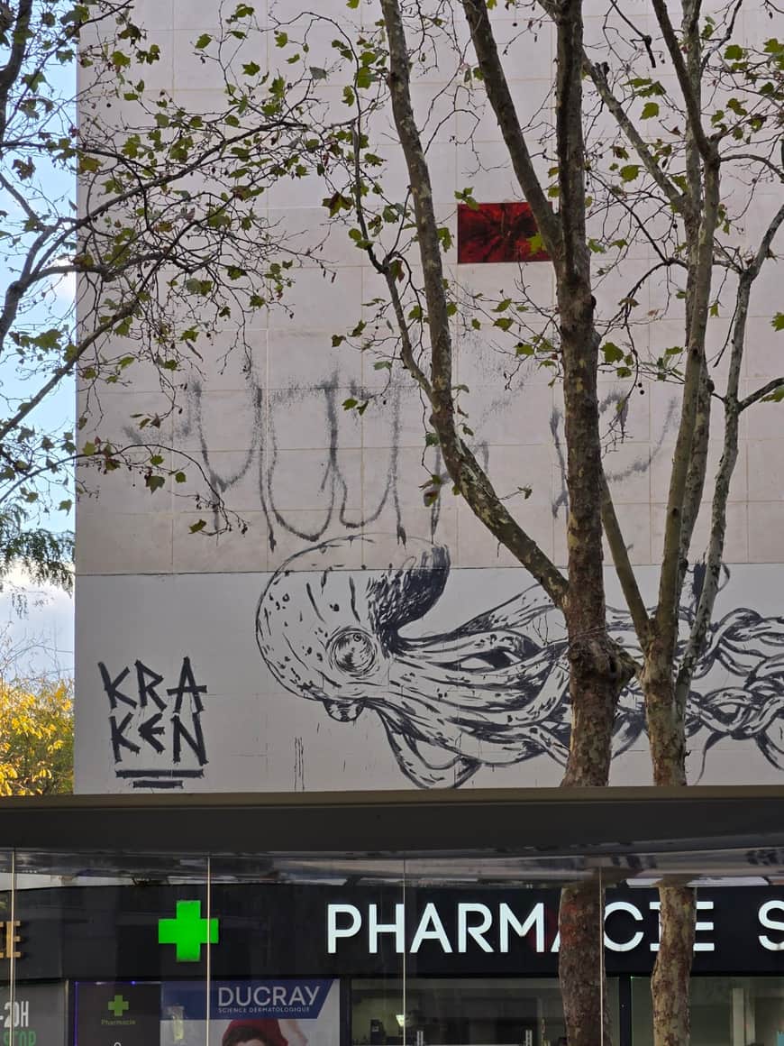 Kraken peint sur une façade blanche au-dessus de l’enseigne d’une pharmacie