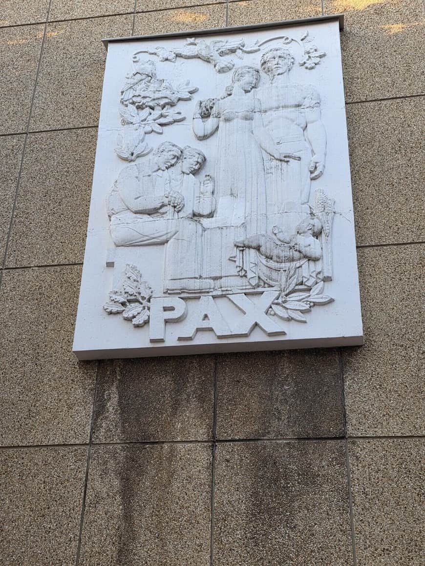 Relief architectural blanc représentant plusieurs figures autour du mot PAX