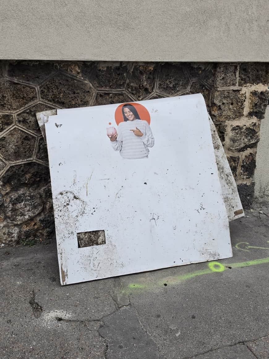 Panneau publicitaire abandonné contre un mur, montrant une femme tenant une tirelire rose
