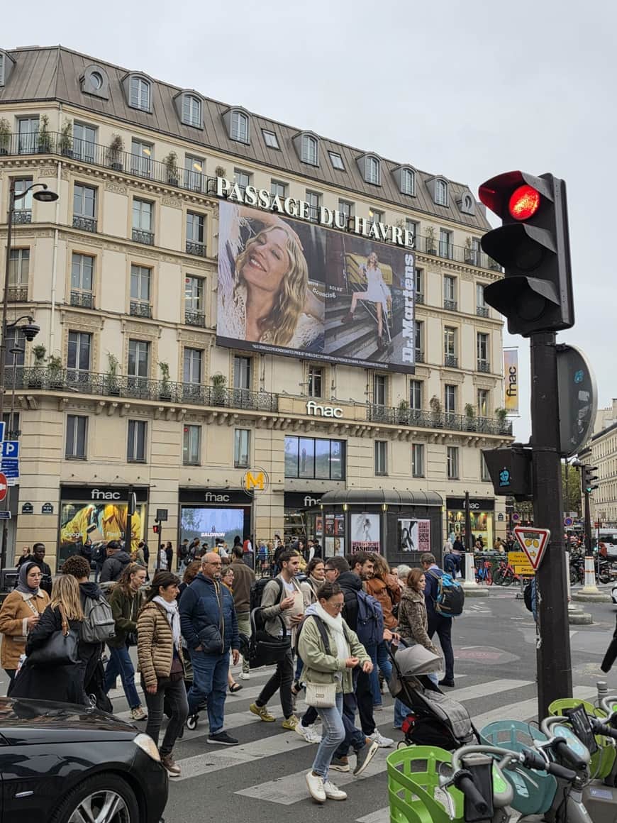 Carrefour animé devant le Passage du Havre, dominé par un portrait publicitaire monumental