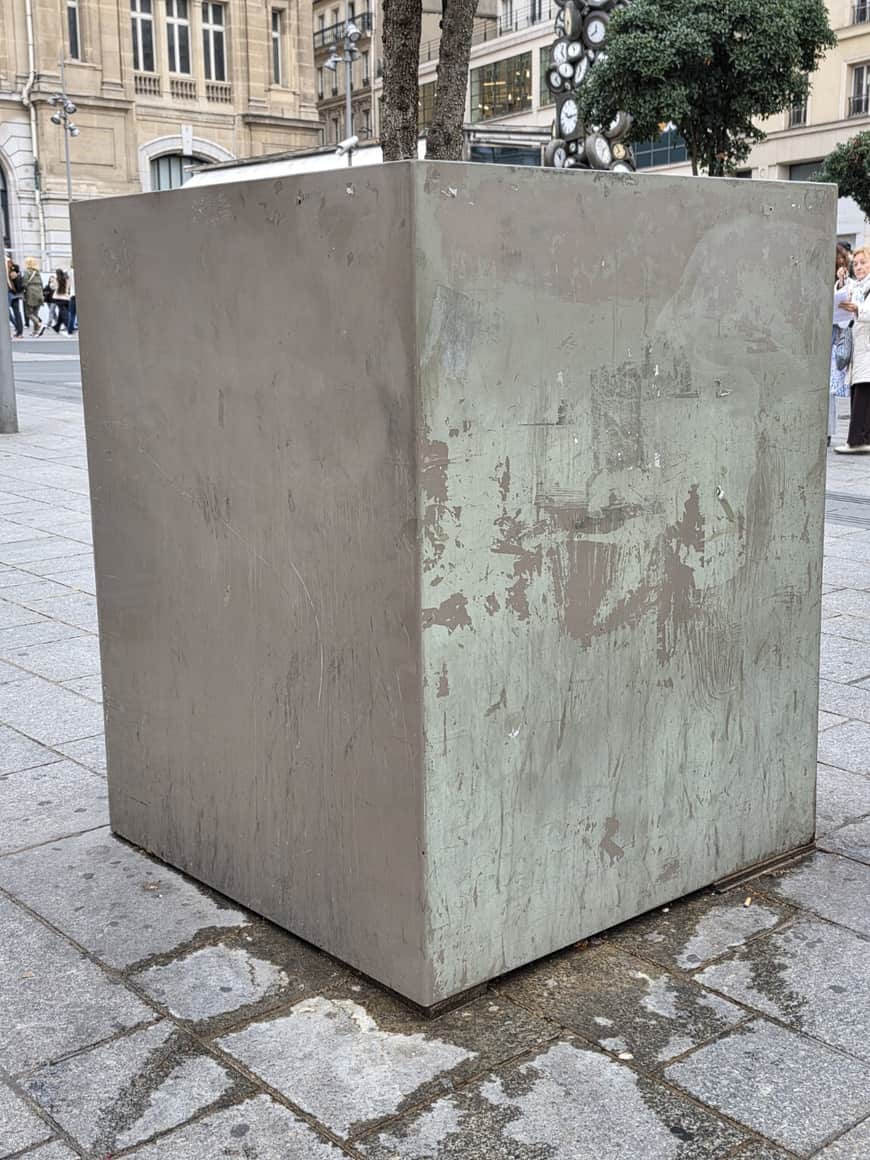 Grand socle cubique vide, marqué et patiné, sur une place publique