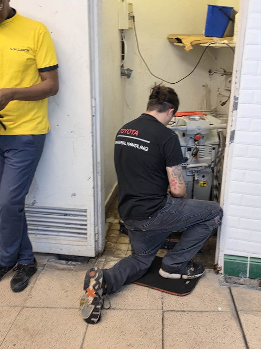 Technicien agenouillé devant une machine ouverte dans l’entrée d’un commerce