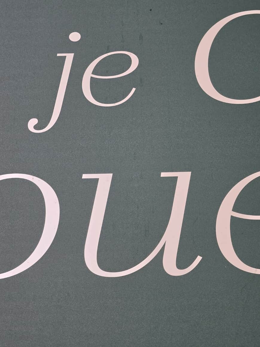 Fragment de grandes lettres roses sur fond gris où se lisent je et une partie du mot joue