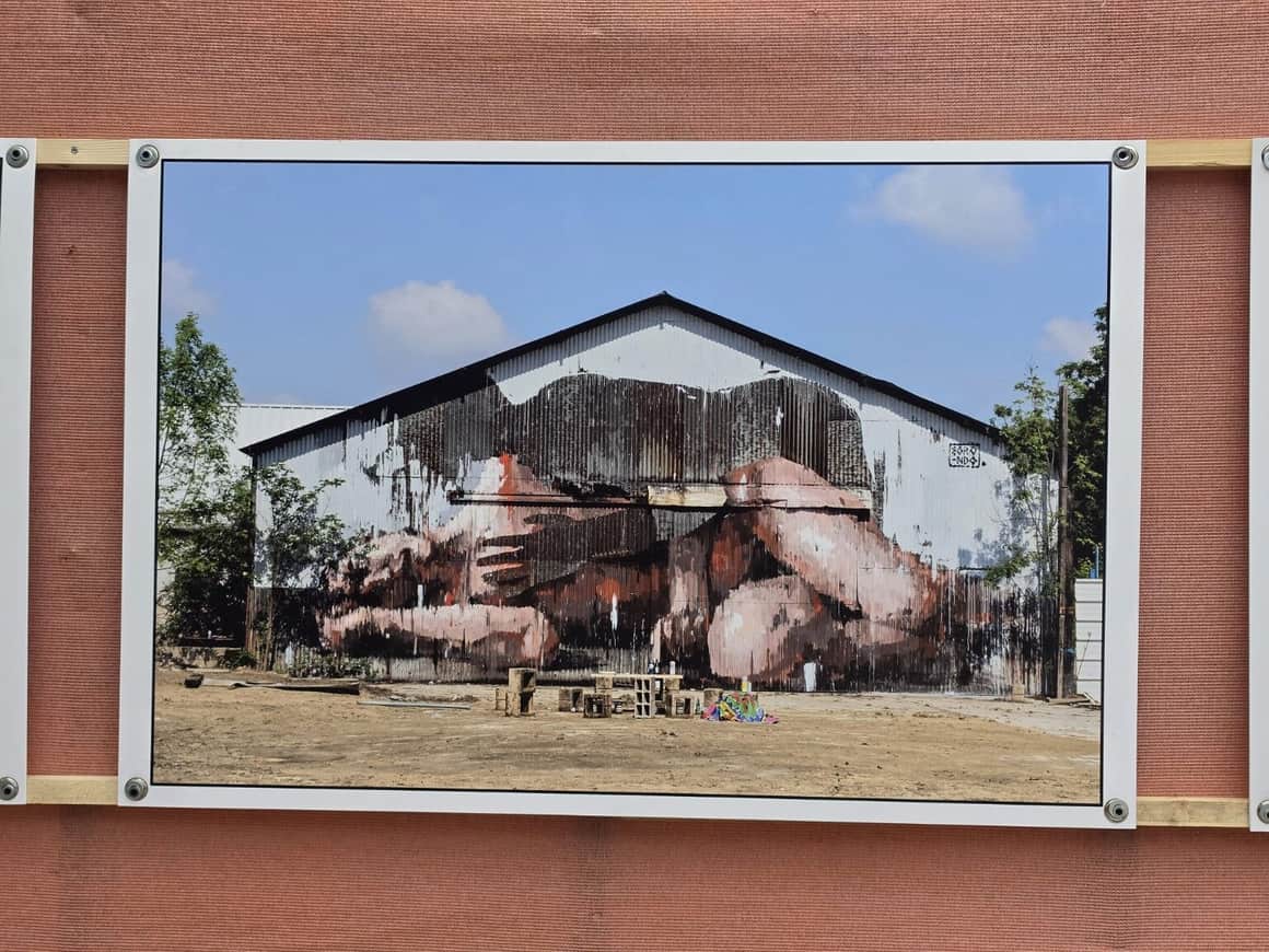 Photographie exposée d’un vaste hangar en tôle peint d’une étreinte monumentale