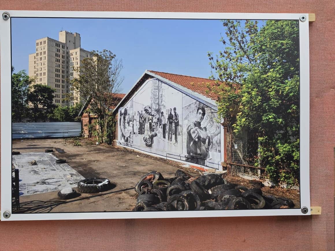 Photographie exposée d’un bâtiment bas couvert d’un montage noir et blanc de personnages, avec pneus au premier plan et tour à l’arrière