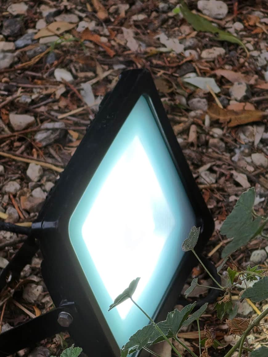 Luminaire extérieur en forme de losange posé parmi les graviers et les feuilles