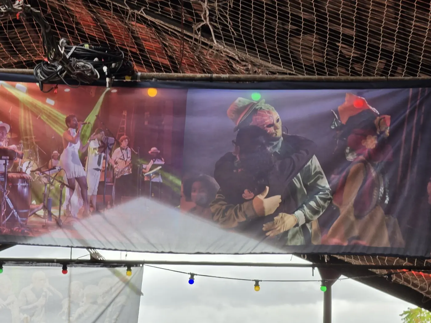 Scène de spectacle reproduite sur une grande toile tendue sous un filet, avec des lumières colorées