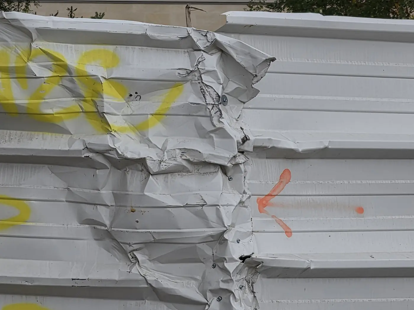Tôle de chantier blanche froissée et déchirée, marquée de traces de peinture jaune et orange