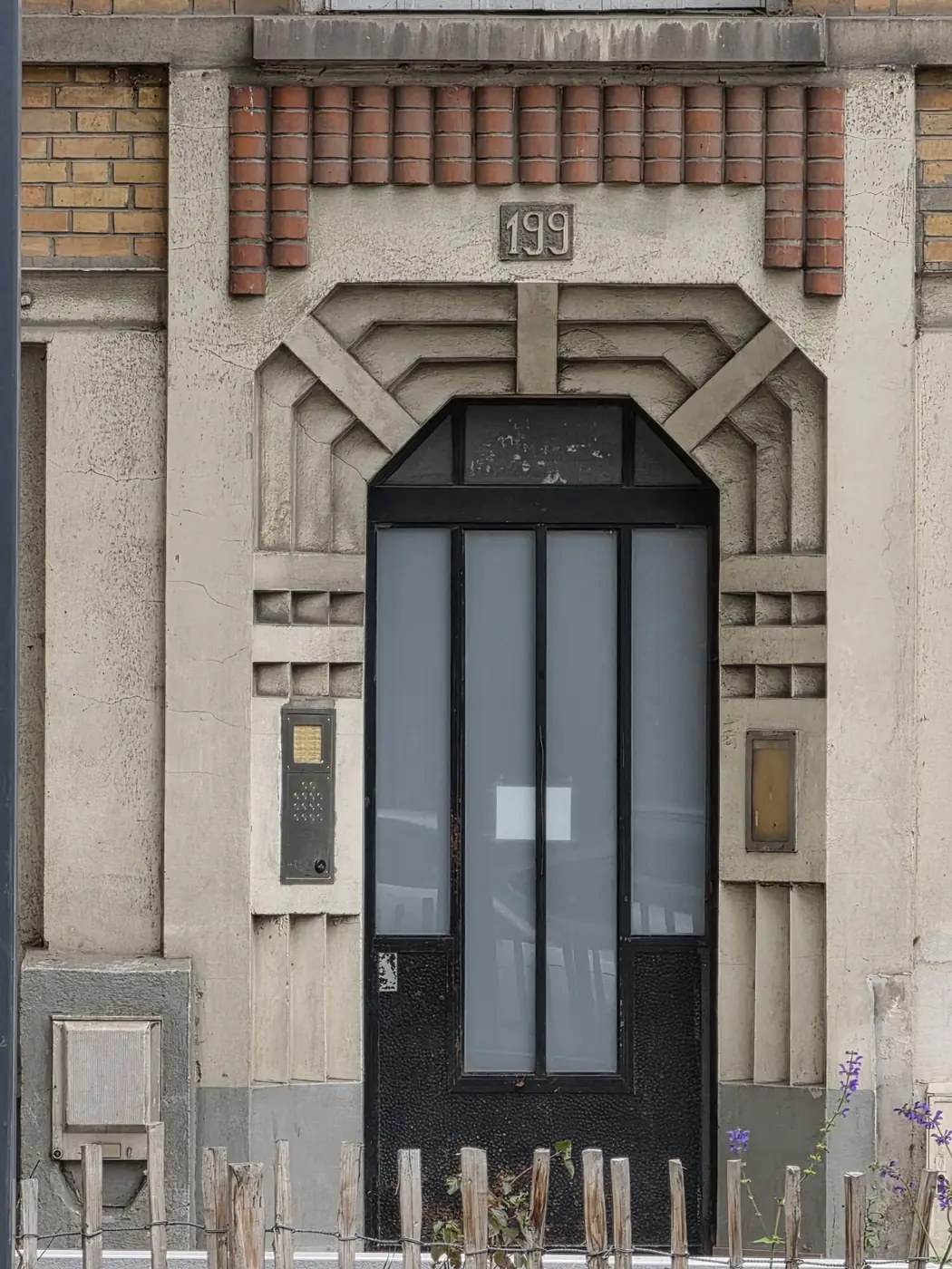 Porte sombre au numéro 199 dans une façade de brique et de pierre à décor géométrique
